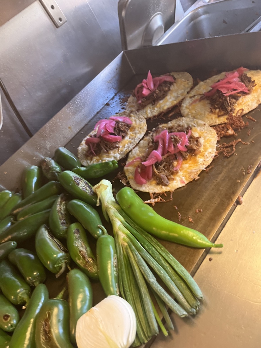Carnitas tacos crisping on the griddle beside fresh jalapeños and green onions