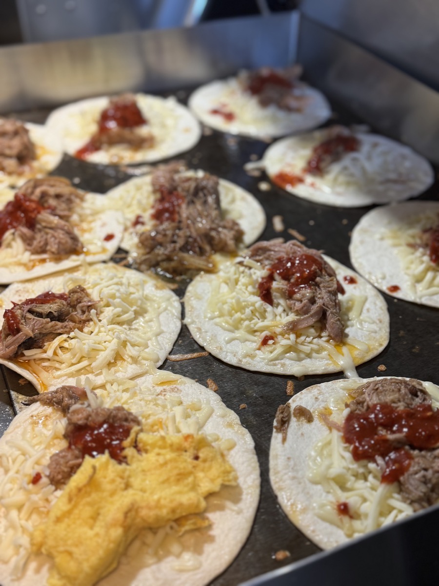 A large batch of carnitas tacos lined up on the griddle