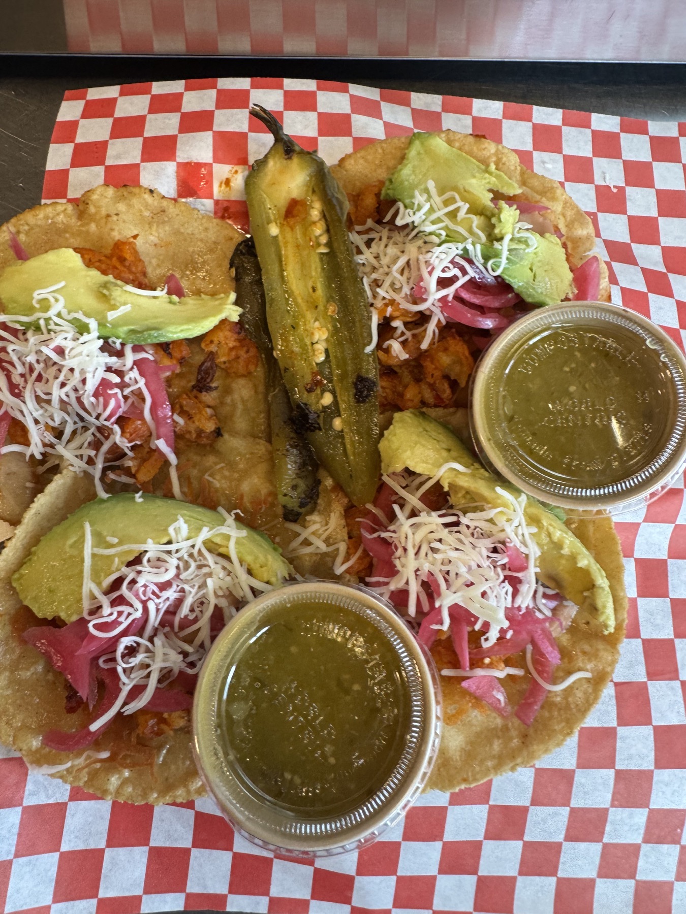 A full taco plate with avocado, cheese, pickled onions, salsa and a grilled jalapeño