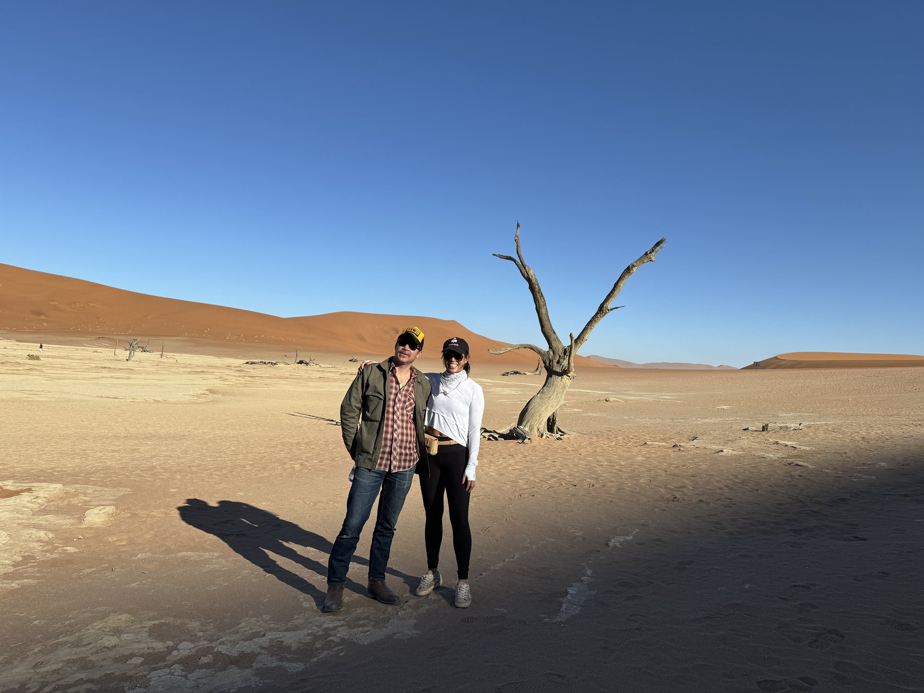Cody and his partner beside a desert tree and red dunes
